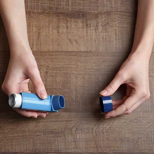 Female hands holding asthma inhaler on wooden background