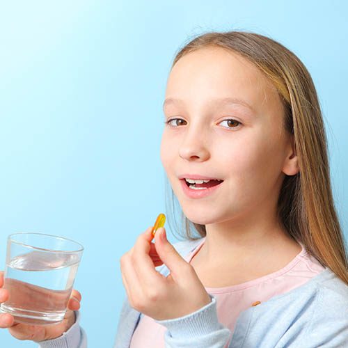 A teenage girl holds an omega 3 capsule in her hands on a colored background. Fish oil, natural supplements. High quality photo