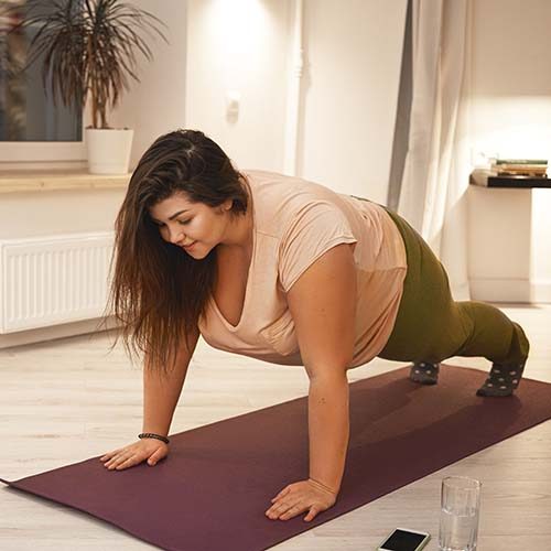 Sports, healthy lifestyle, fitness and obesity concept. Energetic self determined young plus size female in sportswear doing plank exercise on mat. Curvy brunette woman exercising at home, planking